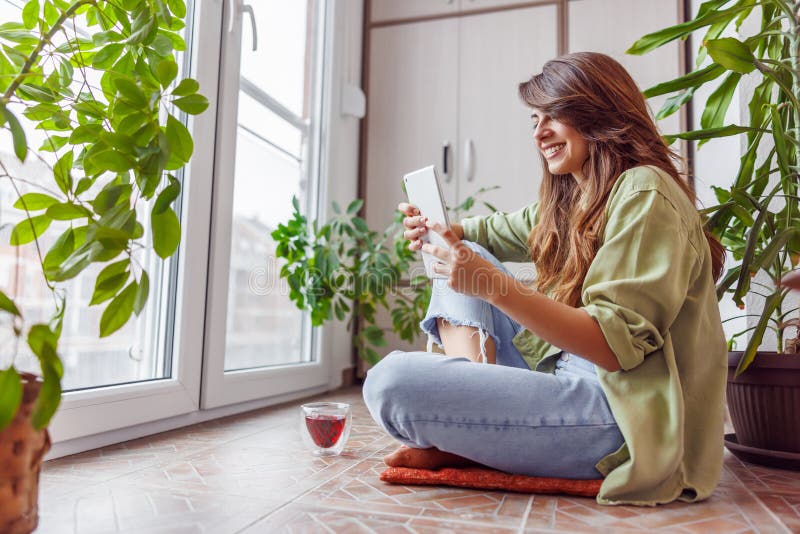 Woman spending leisure time relaxing at home, sitting at her balcony floor drinking tea and reading an ebook using tablet computer. Woman spending leisure time relaxing at home, sitting at her balcony floor drinking tea and reading an ebook using tablet computer