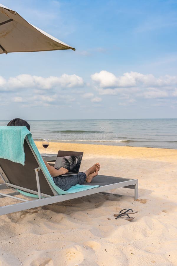 Donna che utilizza computer portatile mentre rilassandosi sulla spiaggia nell'estate fotografie stock Donna che utilizza computer portatile mentre rilassandosi sulla spiaggia nell'estate fotografie stock