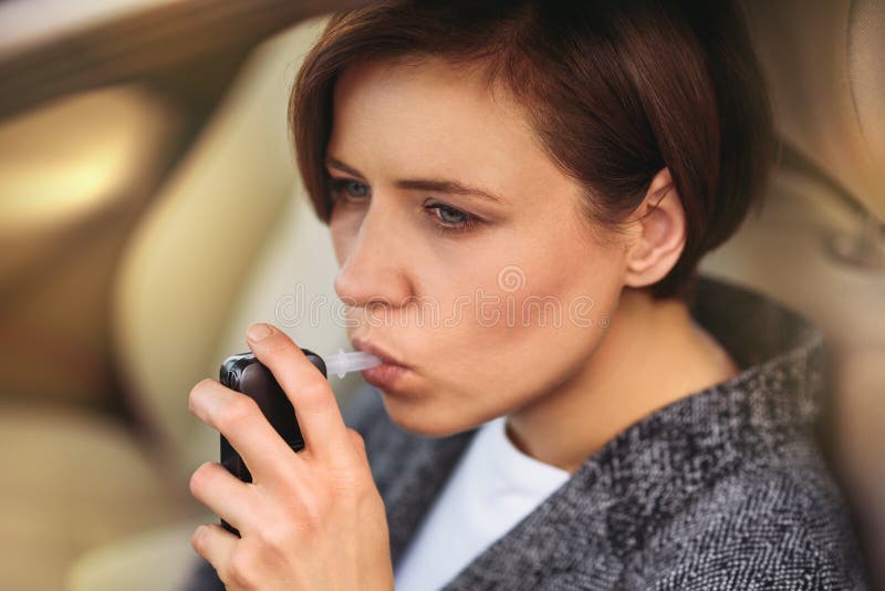 Donna che utilizza l'analizzatore dell'alcool del respiro nell'automobile fotografie stock Donna che utilizza l'analizzatore dell'alcool del respiro nell'automobile fotografie stock