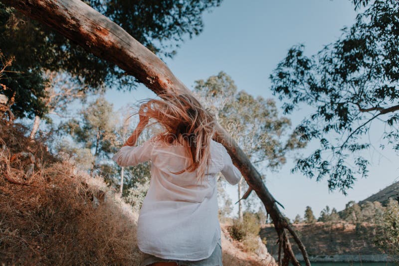 Donna con capelli ventosi che cammina sotto un albero caduto nella foresta immagine stock Donna con capelli ventosi che cammina sotto un albero caduto nella foresta immagine stock