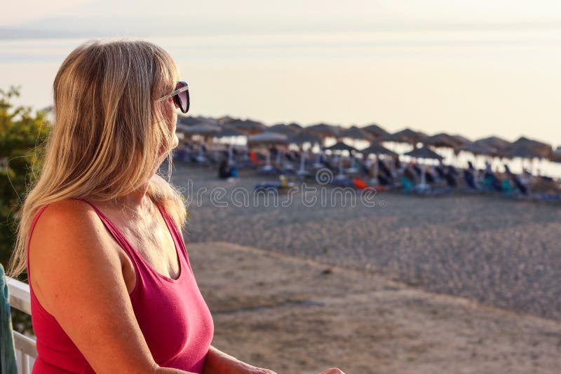 Donna con gli occhiali da sole che stanno sul balcone presto nel Morni fotografia stock Donna con gli occhiali da sole che stanno sul balcone presto nel Morni fotografia stock