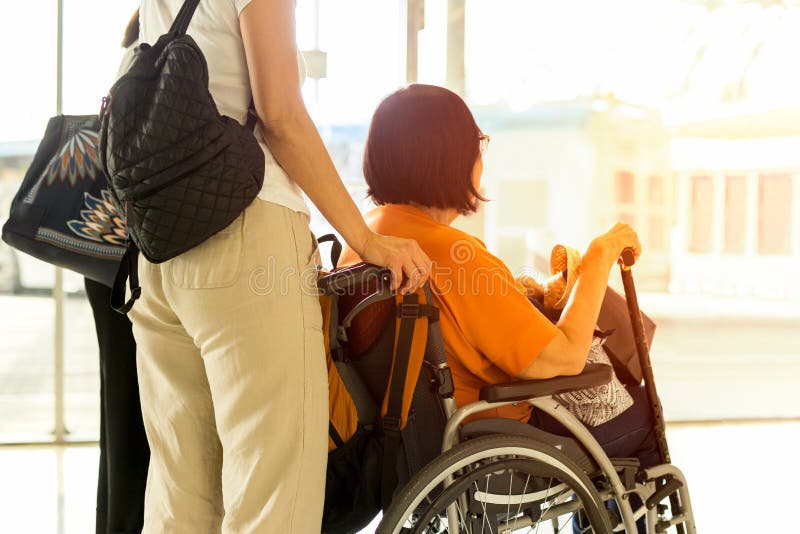 Donna con la madre nell'imbarco aspettante della sedia a rotelle all'aeroporto internazionale immagini stock libere da diritti Donna con la madre nell'imbarco aspettante della sedia a rotelle all'aeroporto internazionale immagini stock libere da diritti