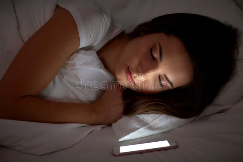 Donna con smartphone che dorme nel letto di notte immagini stock libere da diritti