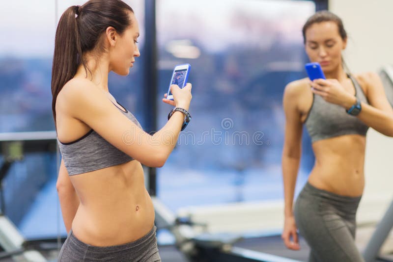 Donna con smartphone che si fa un selfie allo specchio in palestra immagini stock