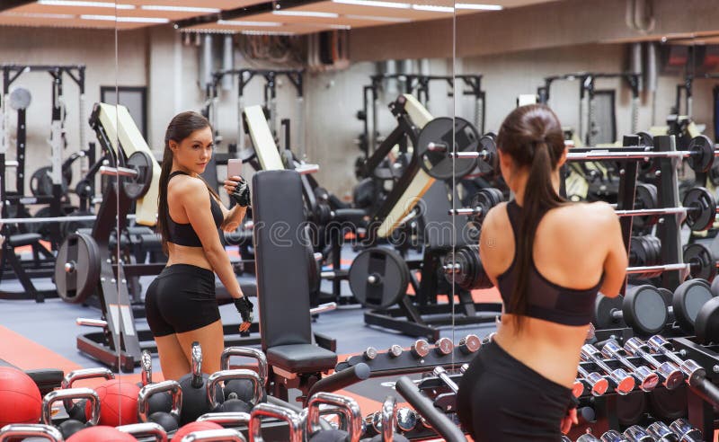 Donna con smartphone che si fa un selfie allo specchio in palestra fotografia stock libera da diritti