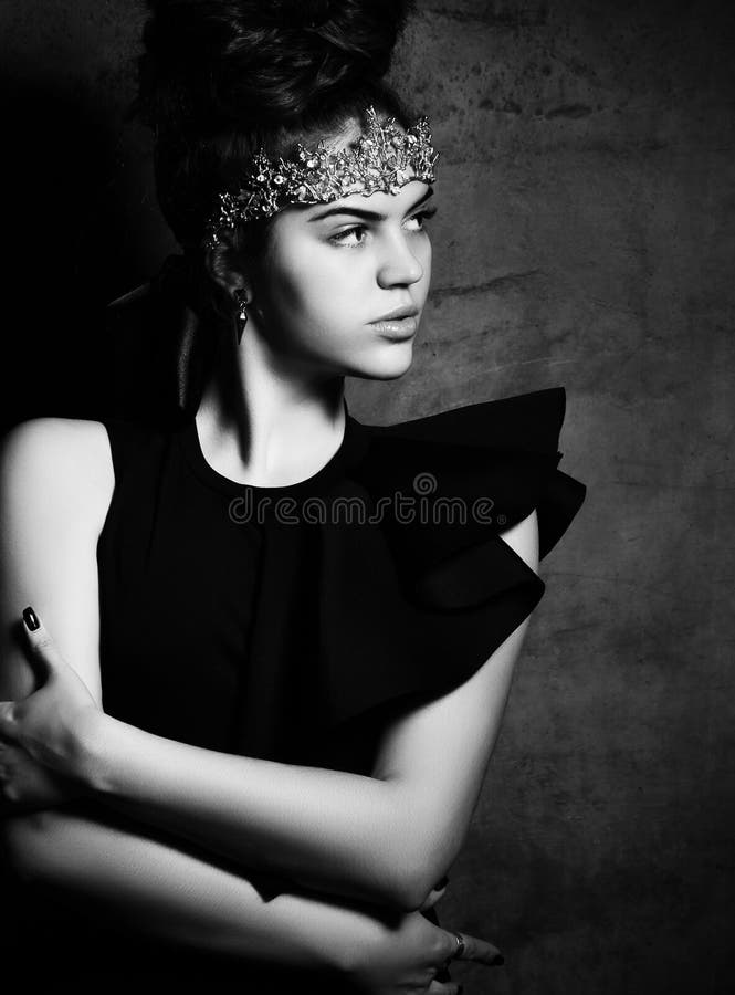 Donna con una corona dorata sulla fronte, in un corpo nero intelligente, calzamaglia di nylon Si abbracciava, posando su sfondo g fotografia stock