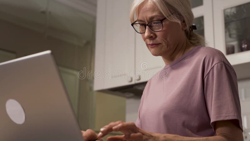 Donna concentrata che usa il computer portatile in cucina moderna video d archivio