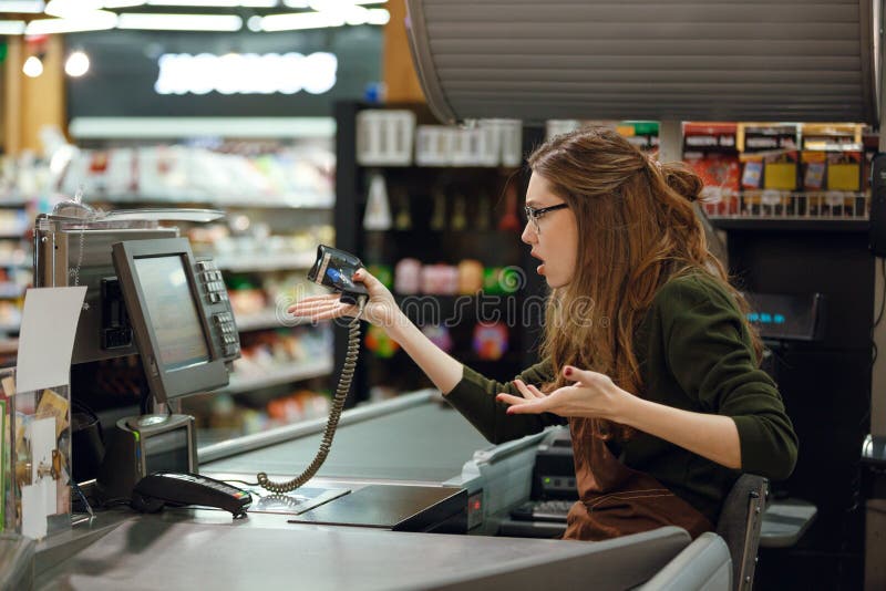 Side view picture of confused cashier woman on workspace in supermarket shop. Looking aside. Side view picture of confused cashier woman on workspace in supermarket shop. Looking aside.