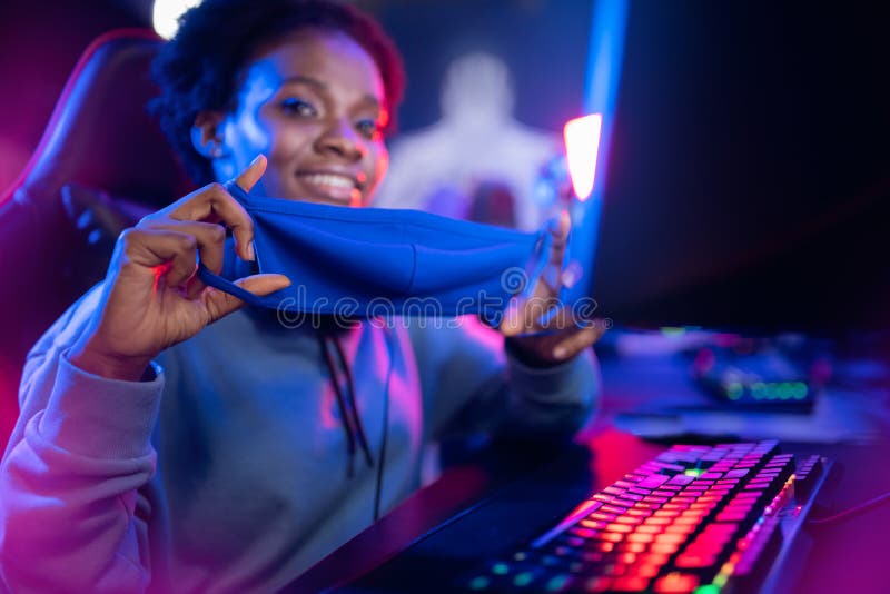 Donna d'azzardo africana con una maschera di sicurezza protegge il coronavirus e l'influenza gioca online con un computer fotografie stock libere da diritti