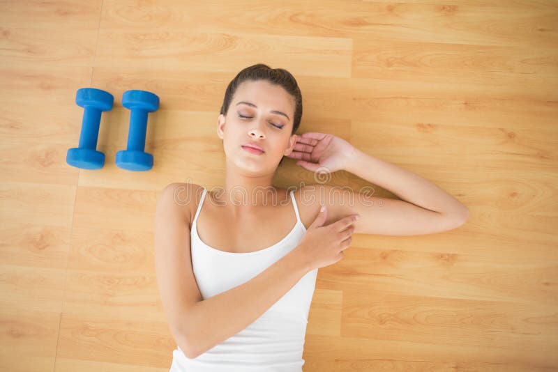 Donna dai capelli marrone naturale pacifica in abiti sportivi bianchi che dorme sul pavimento fotografie stock libere da diritti Donna dai capelli marrone naturale pacifica in abiti sportivi bianchi che dorme sul pavimento fotografie stock libere da diritti