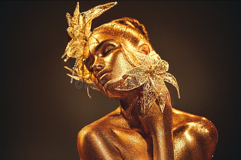 Donna del modello dell'oro di modo con le scintille dorate luminose su pelle che posa, fiore di fantasia Ritratto di bella ragazz fotografia stock libera da diritti Donna del modello dell'oro di modo con le scintille dorate luminose su pelle che posa, fiore di fantasia Ritratto di bella ragazz fotografia stock libera da diritti