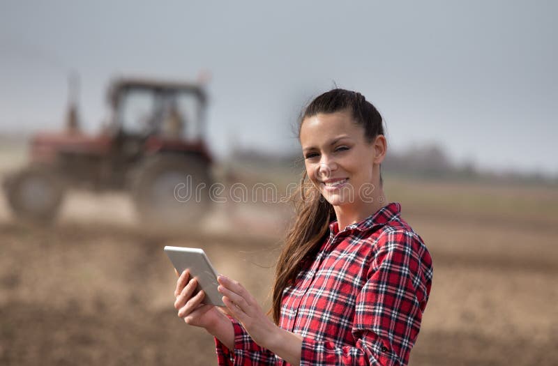 Donna dell'agricoltore con la compressa ed il trattore nel campo immagine stock libera da diritti Donna dell'agricoltore con la compressa ed il trattore nel campo immagine stock libera da diritti