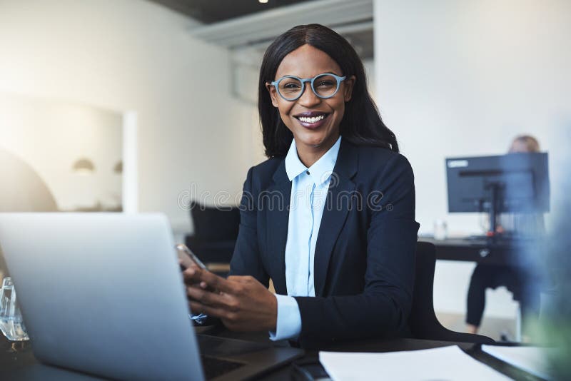 Donna di affari afroamericana sorridente che per mezzo di un cellulare lei immagine stock Donna di affari afroamericana sorridente che per mezzo di un cellulare lei immagine stock