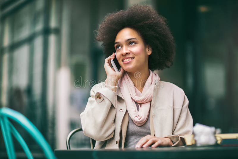 Donna di affari afroamericana sorridente giovane che rivolge allo smartphone fotografia stock Donna di affari afroamericana sorridente giovane che rivolge allo smartphone fotografia stock