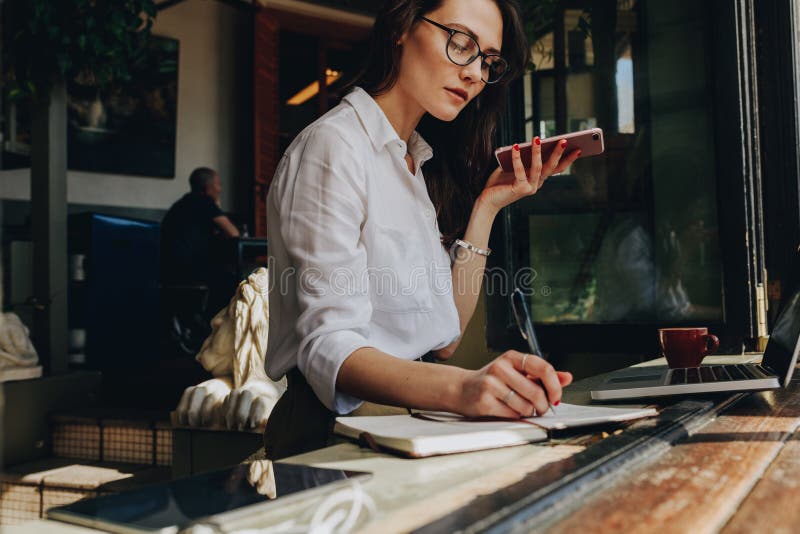 Donna di affari che parla sul telefono e che fa le note al caffè immagini stock Donna di affari che parla sul telefono e che fa le note al caffè immagini stock
