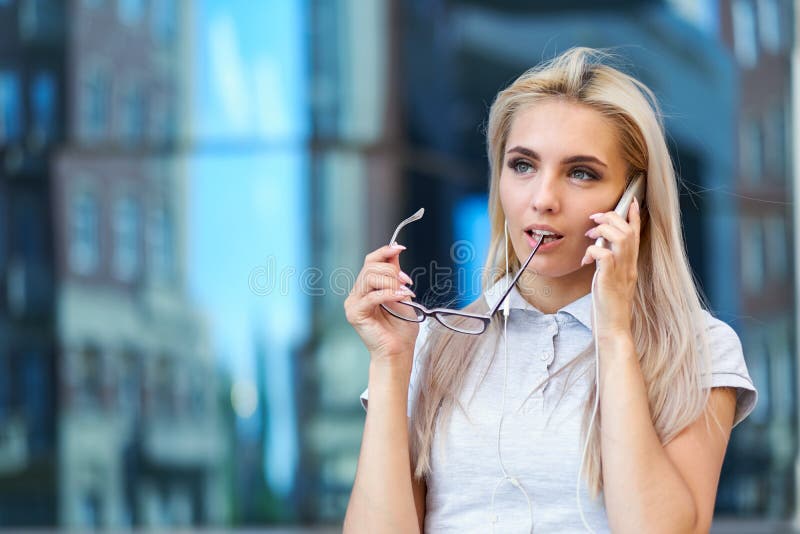 Donna di affari che parla sul telefono, tenente i vetri Ritratto di bella ragazza su fondo urbano blu immagini stock Donna di affari che parla sul telefono, tenente i vetri Ritratto di bella ragazza su fondo urbano blu immagini stock