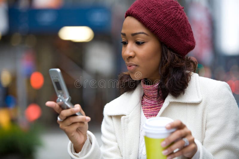 An attractive African American business woman checks her cell phone in the city. She could be text messaging or even browsing the web via wi-fi or 4G connection. An attractive African American business woman checks her cell phone in the city. She could be text messaging or even browsing the web via wi-fi or 4G connection.