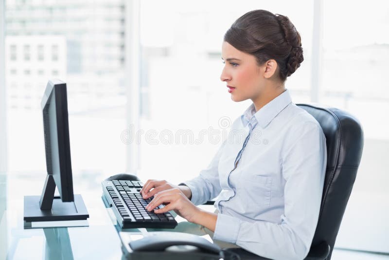 Donna di affari dai capelli marrone di classe concentrata che scrive su un computer fotografia stock libera da diritti Donna di affari dai capelli marrone di classe concentrata che scrive su un computer fotografia stock libera da diritti