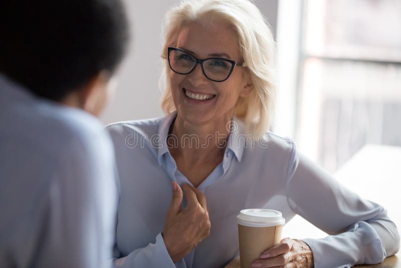 Donna di affari matura emozionante che parla con il collega durante la pausa caffè