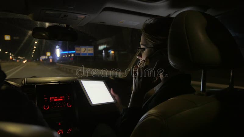 Donna di affari nell'automobile che parla sul telefono Guida nell'automobile sulla strada di notte