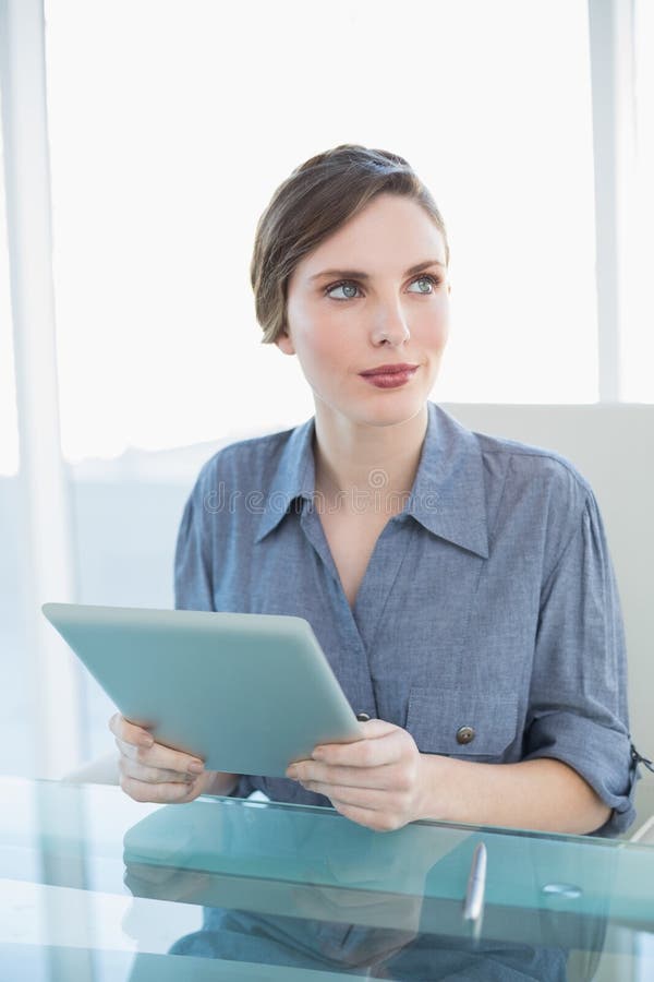 Donna di affari splendida che tiene la sua compressa mentre sedendosi al suo scrittorio immagini stock Donna di affari splendida che tiene la sua compressa mentre sedendosi al suo scrittorio immagini stock