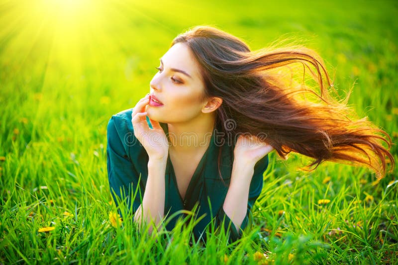 Donna di bellezza che si trova sul campo che gode della natura Bella ragazza castana con i capelli lunghi sani di volo immagine stock Donna di bellezza che si trova sul campo che gode della natura Bella ragazza castana con i capelli lunghi sani di volo immagine stock