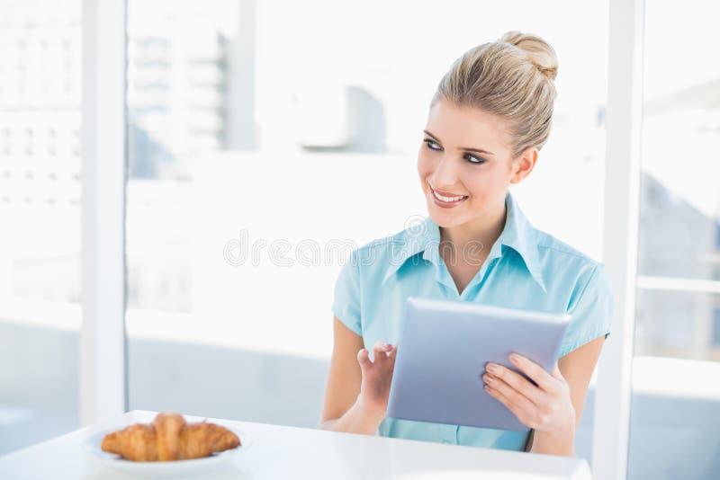 Donna di classe allegra che per mezzo della compressa mentre mangiando prima colazione fotografia stock libera da diritti Donna di classe allegra che per mezzo della compressa mentre mangiando prima colazione fotografia stock libera da diritti