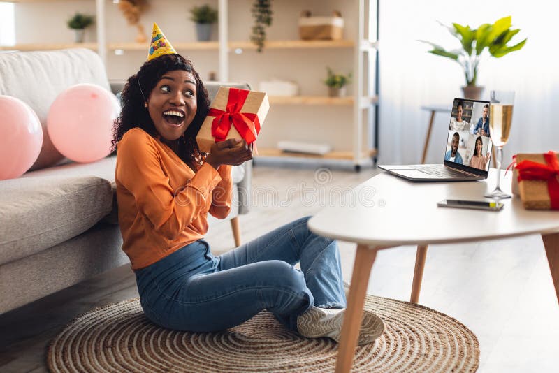 Donna di colore riceve un regalo con una festa di compleanno online a casa immagini stock