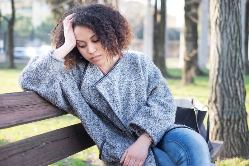 Donna di colore triste messa da solo su un banco fotografia stock libera da diritti Donna di colore triste messa da solo su un banco fotografia stock libera da diritti