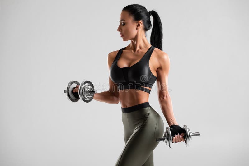 Donna di forma fisica che fa esercizio per il bicipite su fondo grigio Allenamento muscolare della donna con le teste di legno immagini stock