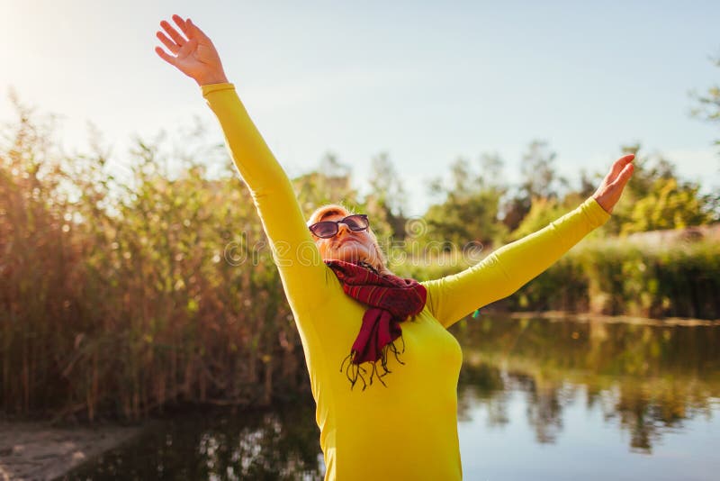 Donna di mezza età che si sente libero e felice sulla sponda del fiume il giorno di autunno Signora senior che solleva le mani su fotografie stock libere da diritti Donna di mezza età che si sente libero e felice sulla sponda del fiume il giorno di autunno Signora senior che solleva le mani su fotografie stock libere da diritti
