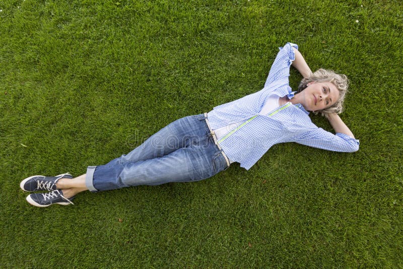 Donna di mezza età felice in abbigliamento casuale di fine settimana che si rilassa sull'erba in un parco