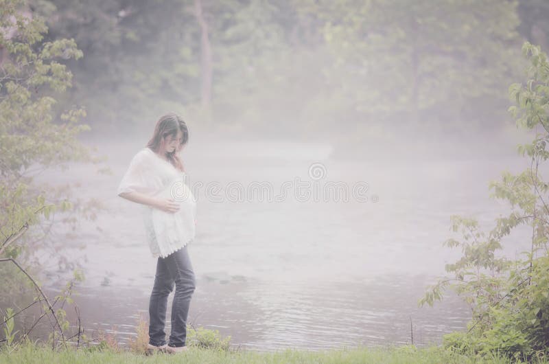 Pregnant woman outdoors by a foggy river on a peaceful morning. Pregnant woman outdoors by a foggy river on a peaceful morning.