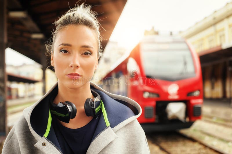 Donna elegante con le cuffie che aspettano un treno allo sta ferroviario fotografia stock Donna elegante con le cuffie che aspettano un treno allo sta ferroviario fotografia stock