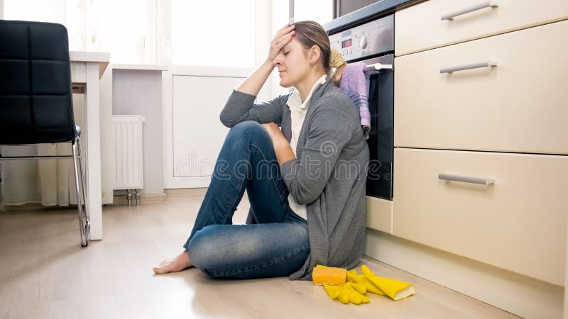 Donna esaurita che si siede sul pavimento alla cucina dopo avere fatto piazza pulita