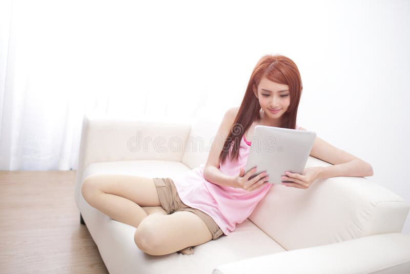 Donna felice che per mezzo del pc della compressa sul sofà fotografia stock libera da diritti Donna felice che per mezzo del pc della compressa sul sofà fotografia stock libera da diritti