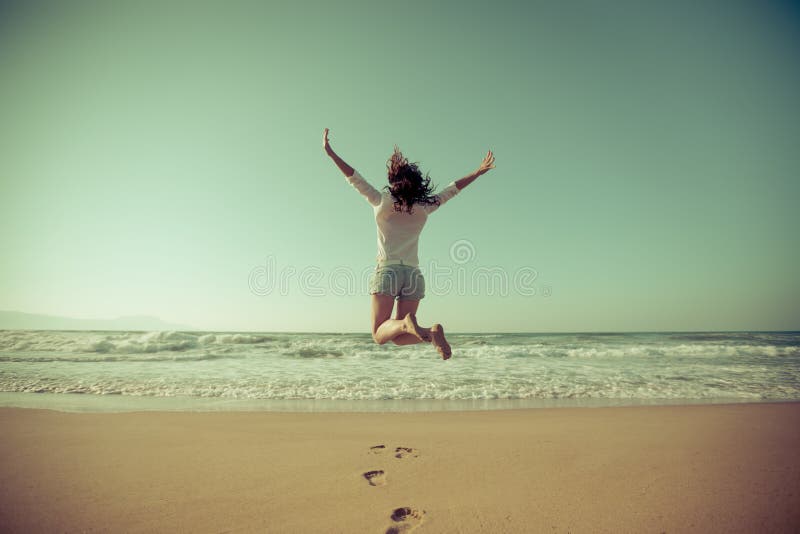 Donna felice che salta alla spiaggia fotografia stock Donna felice che salta alla spiaggia fotografia stock
