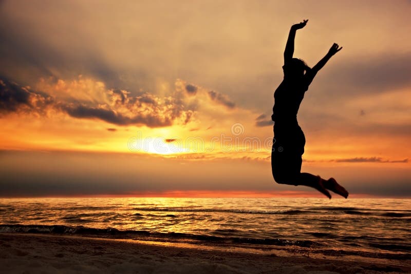 Donna felice che salta sulla spiaggia al tramonto fotografie stock libere da diritti