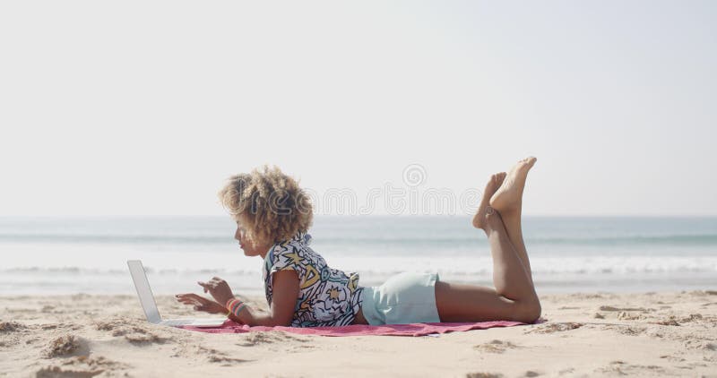 Donna felice che scrive su un computer portatile su una spiaggia archivi video