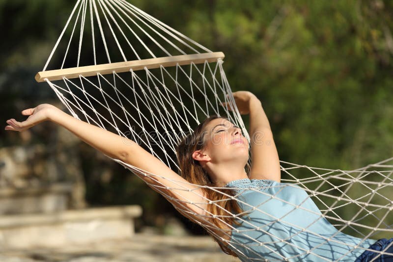 Donna felice che si rilassa su un'amaca in vacanza e che alza armi fotografie stock libere da diritti