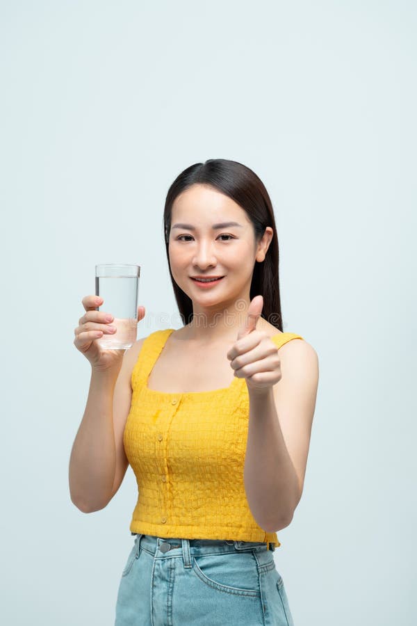 Donna felice che tiene in mano un bicchiere d'acqua e dà i pollici fotografia stock