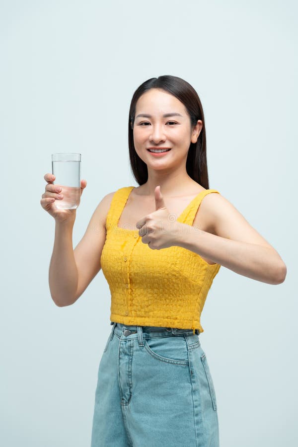 Donna felice che tiene in mano un bicchiere d'acqua e dà i pollici fotografia stock libera da diritti