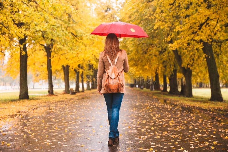 Donna felice con l'ombrello rosso che cammina alla pioggia nel bello parco di autunno fotografia stock Donna felice con l'ombrello rosso che cammina alla pioggia nel bello parco di autunno fotografia stock