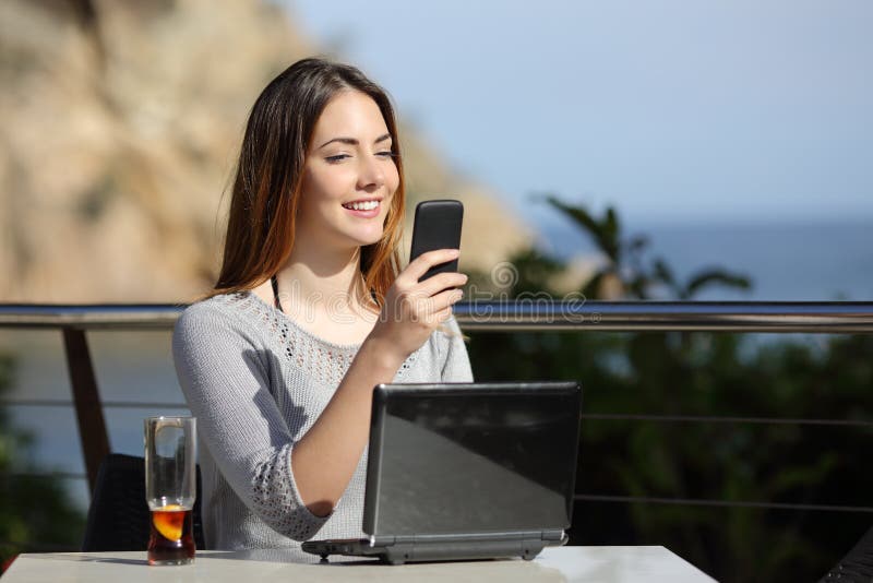 Donna felice in un ristorante con un computer e sul telefono fotografia stock Donna felice in un ristorante con un computer e sul telefono fotografia stock