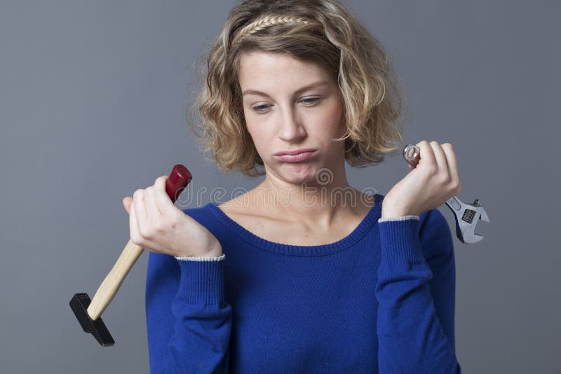 Female DIY concept - disinterested young blond woman bored at holding spanner and hammer as symbols of manual work and mechanics handiwork. Female DIY concept - disinterested young blond woman bored at holding spanner and hammer as symbols of manual work and mechanics handiwork