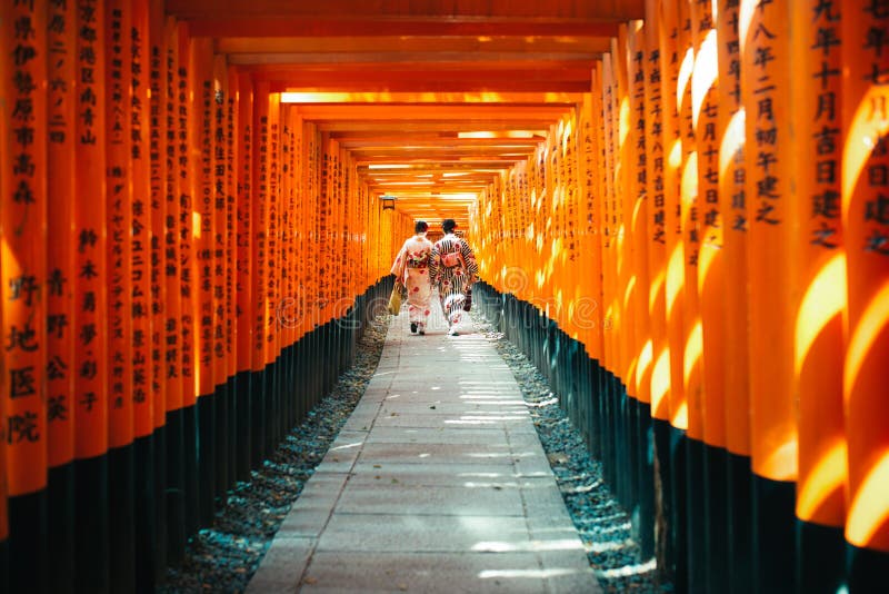 Donna giapponese in vestito dal kimono fra Tori Gate di legno rossa a Fus fotografie stock libere da diritti Donna giapponese in vestito dal kimono fra Tori Gate di legno rossa a Fus fotografie stock libere da diritti