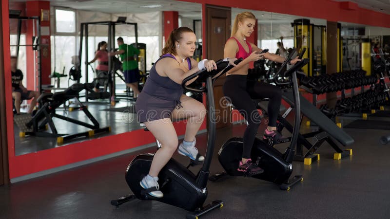Donna grassottella che lavora duro alla bici fissa per raggiungere i risultati, forma fisica, sport immagine stock libera da diritti Donna grassottella che lavora duro alla bici fissa per raggiungere i risultati, forma fisica, sport immagine stock libera da diritti