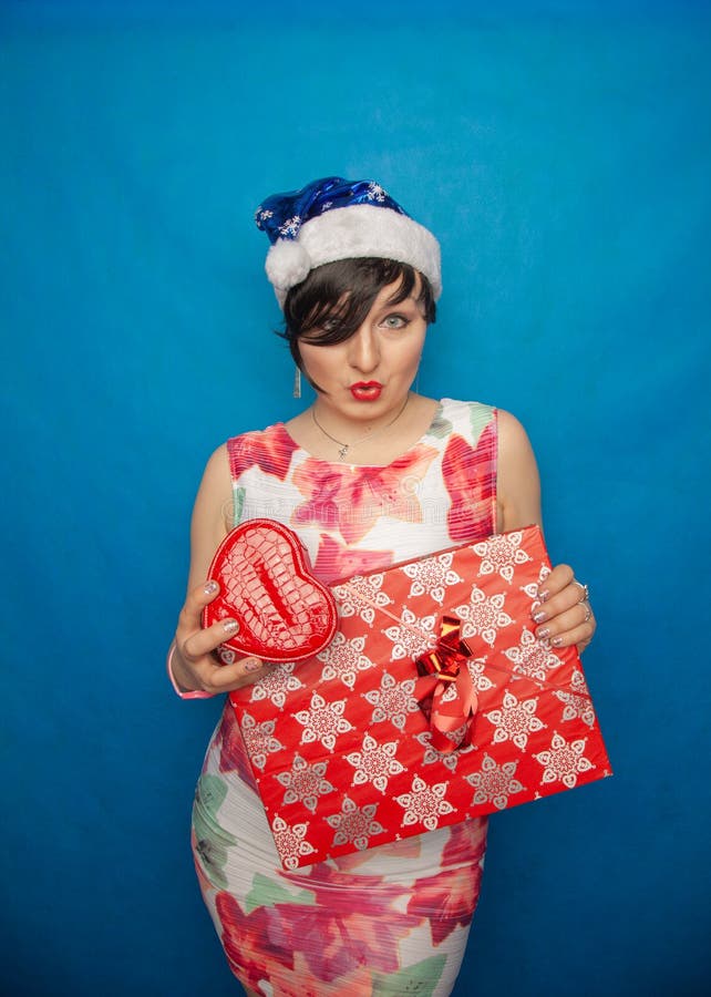 Donna grassottella con la breve condizione del cappello di Santa e dei capelli neri in vestito bianco con i contenitori di regalo fotografia stock Donna grassottella con la breve condizione del cappello di Santa e dei capelli neri in vestito bianco con i contenitori di regalo fotografia stock