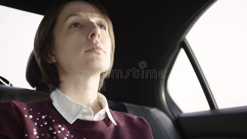 Donna graziosa con capelli marroni in blusa bianca e nella guida marrone rossiccio del maglione in automobile e nell'esame della