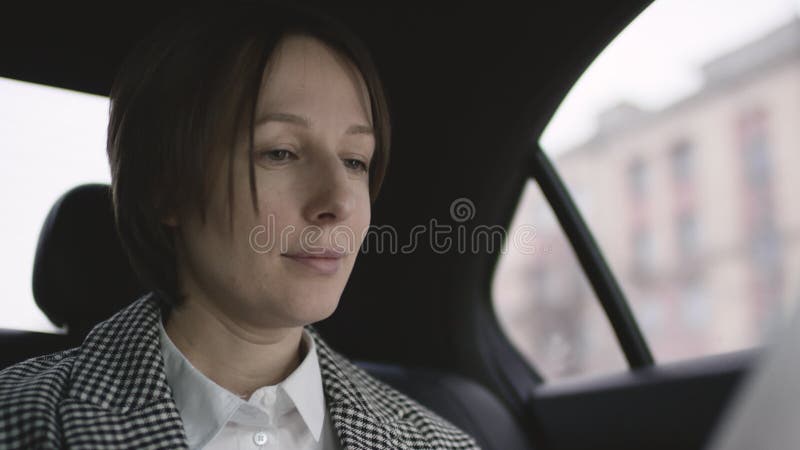 Donna graziosa con capelli marroni nella guida bianca del cappotto del controllo e della blusa nei documenti di lavoro di studio